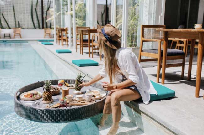 a woman sitting on a pool edge with a tray of food