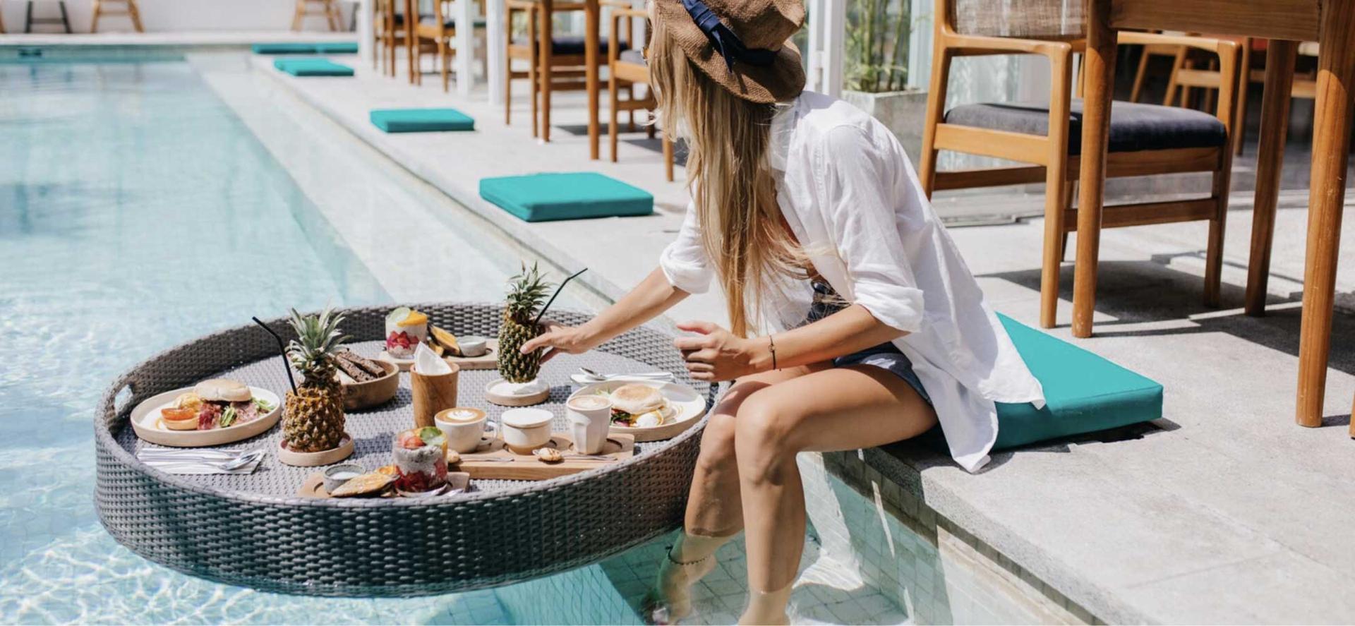 a woman sitting on a pool edge with a tray of food