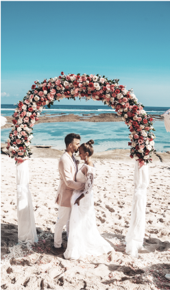 a man and woman standing on a beach under a floral arch