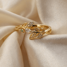 a gold ring with leaves and diamonds on a white fabric