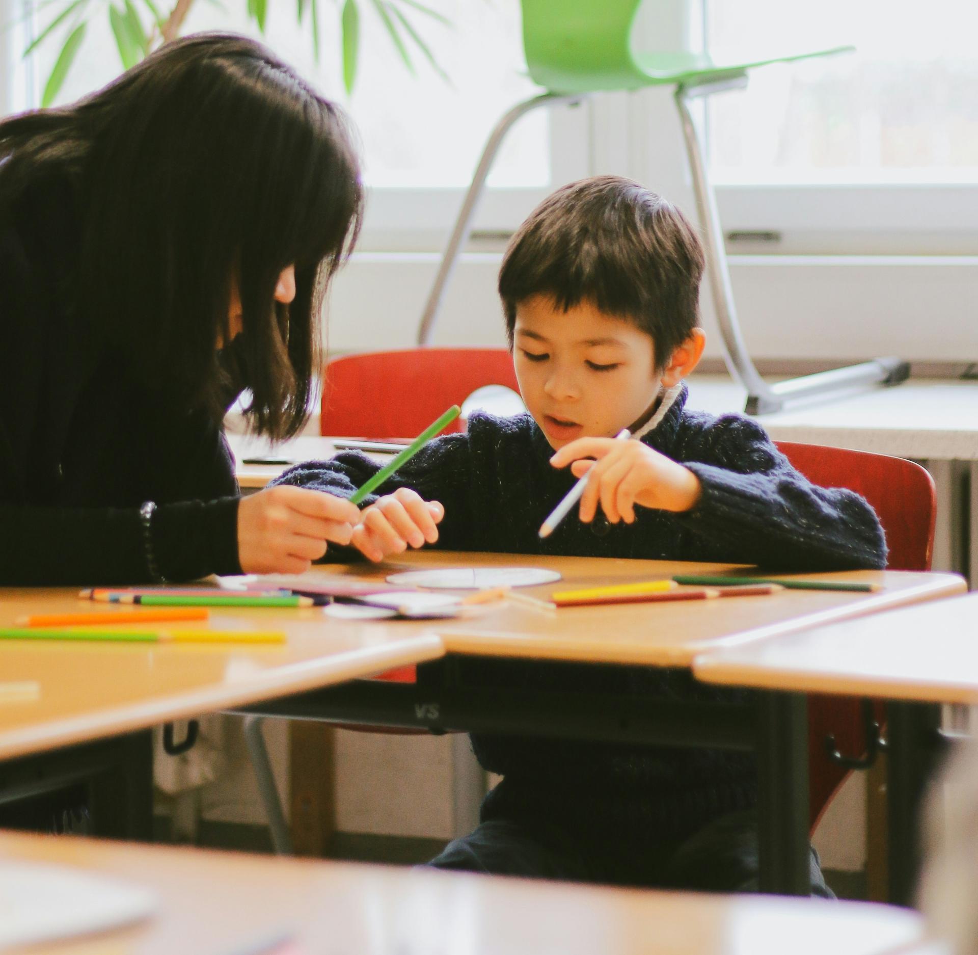 a woman and a boy sitting at a table with colored pencils
