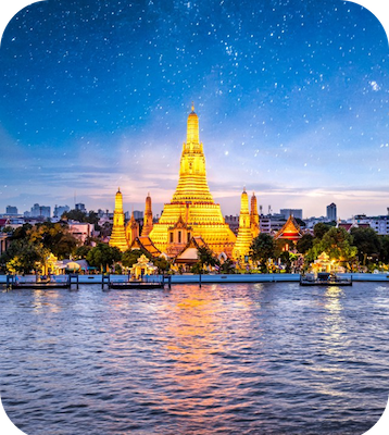 a large building with lights on it by a body of water with Wat Arun in the background