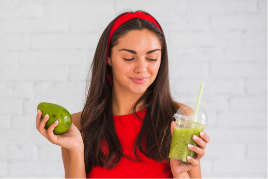 a woman holding a green smoothie and a fruit