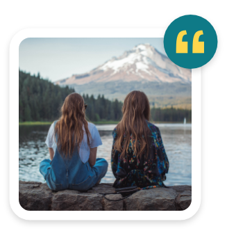 two women sitting on a rock by a lake