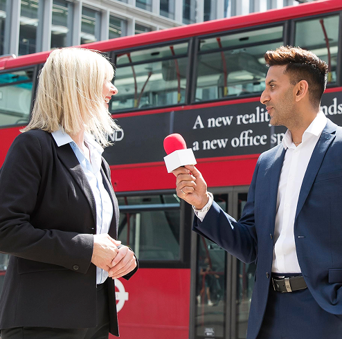 a man and woman holding microphones in front of a bus