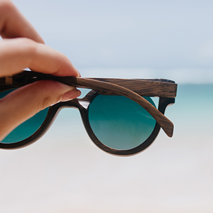 a hand holding sunglasses with blue lenses